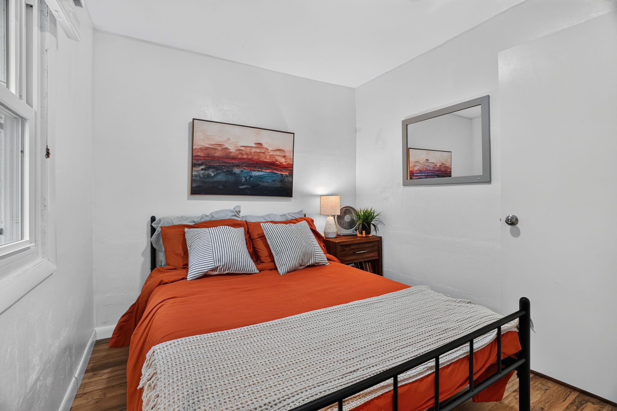 A bedroom with a bed, a bedside table with a lamp, and two paintings on the wall.