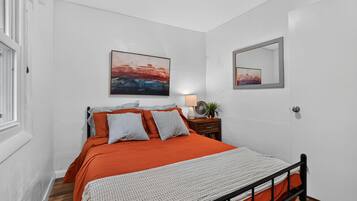 A bedroom with a bed, a bedside table with a lamp, and two paintings on the wall.