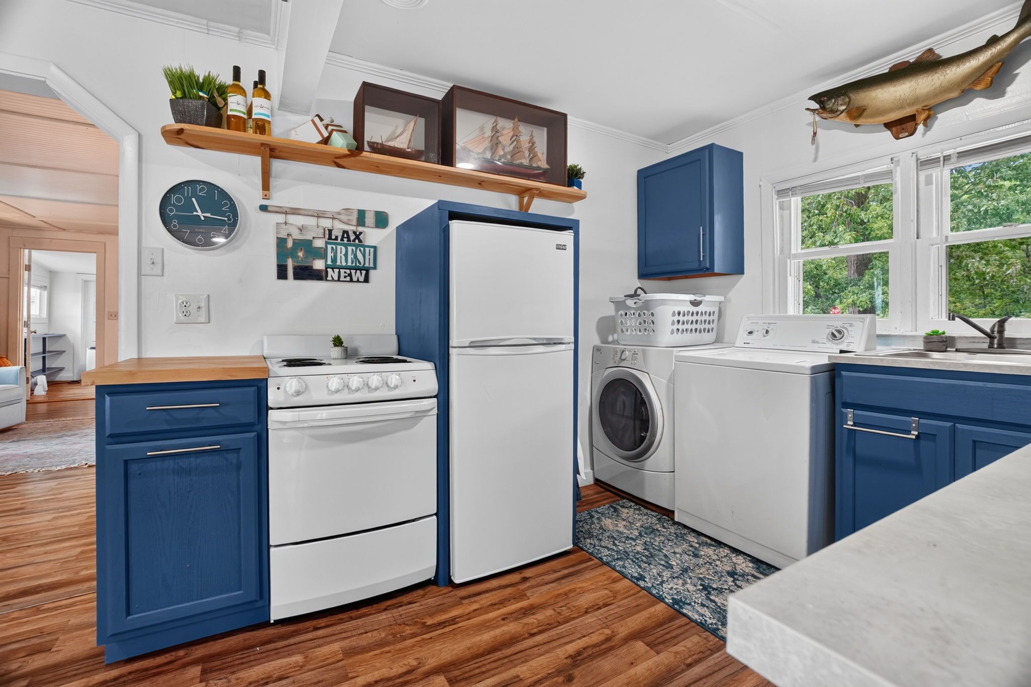 A modern kitchen with a stove, refrigerator, washing machine, and a clock on the wall.