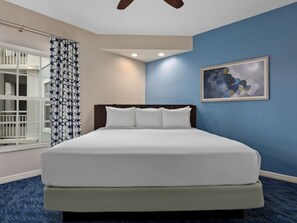 Une chambre d’hôtel avec un lit, un ventilateur de plafond, une fenêtre avec des rideaux et un tableau au mur.