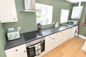 A kitchen with a modern stove, a microwave, a toaster, and a washing machine. - Thwaite Hill Barn, Thornthwaite -  with garden, parking and wood burning stove (Thornthwaite)