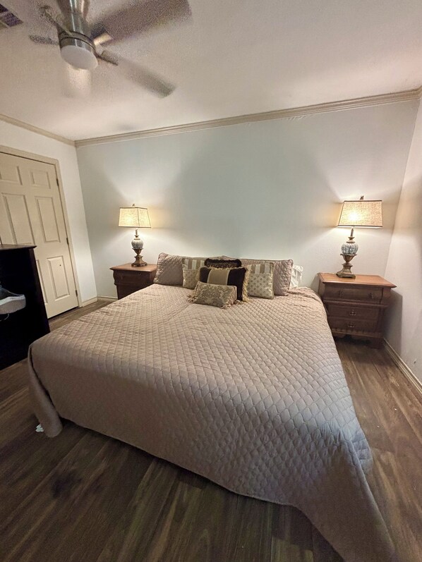 A bedroom with a large bed, two bedside tables with lamps, a ceiling fan, and a door.
