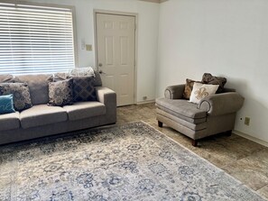 A living room with a grey sofa and armchair, patterned rug, and a closed door.