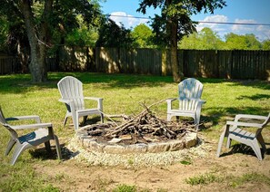A backyard with a fire pit surrounded by Adirondack chairs.