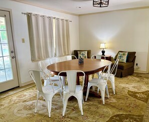 A dining area with a round table, white chairs, a brown sofa, and a patterned carpet.