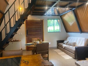 Una sala de estar moderna con una escalera de madera, un comedor con una mesa y sillas, y un sofá.