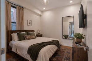 A bedroom with a bed, bedside table, lamp, mirror, and a potted plant. - Sprawling Townhome in the Heart of NYC (New York)