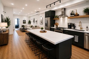 A modern kitchen with a central island, bar stools, stainless steel appliances, and a dining area with a sofa and chairs. - Sprawling Townhome in the Heart of NYC (New York)