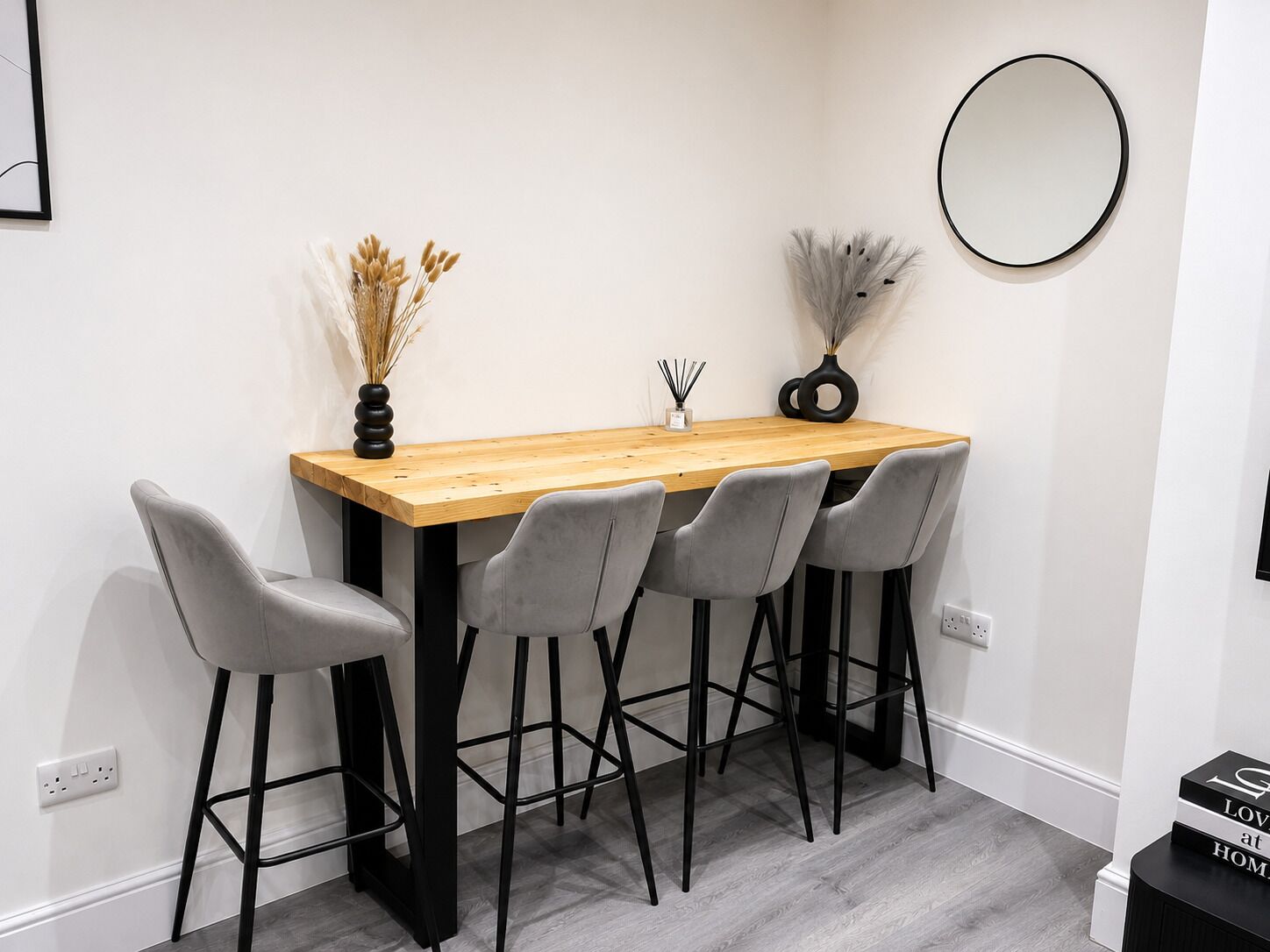 Een eethoek met een houten tafel, vier grijze stoelen en een ronde spiegel aan de muur.
