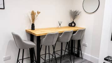 Een eethoek met een houten tafel, vier grijze stoelen en een ronde spiegel aan de muur.