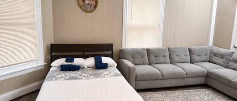 A bedroom with a bed, a gray sofa, a patterned rug, and a decorative mirror.