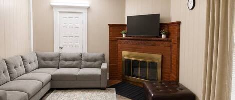 A living room with a sectional sofa, a fireplace, a television, and a clock on the wall.