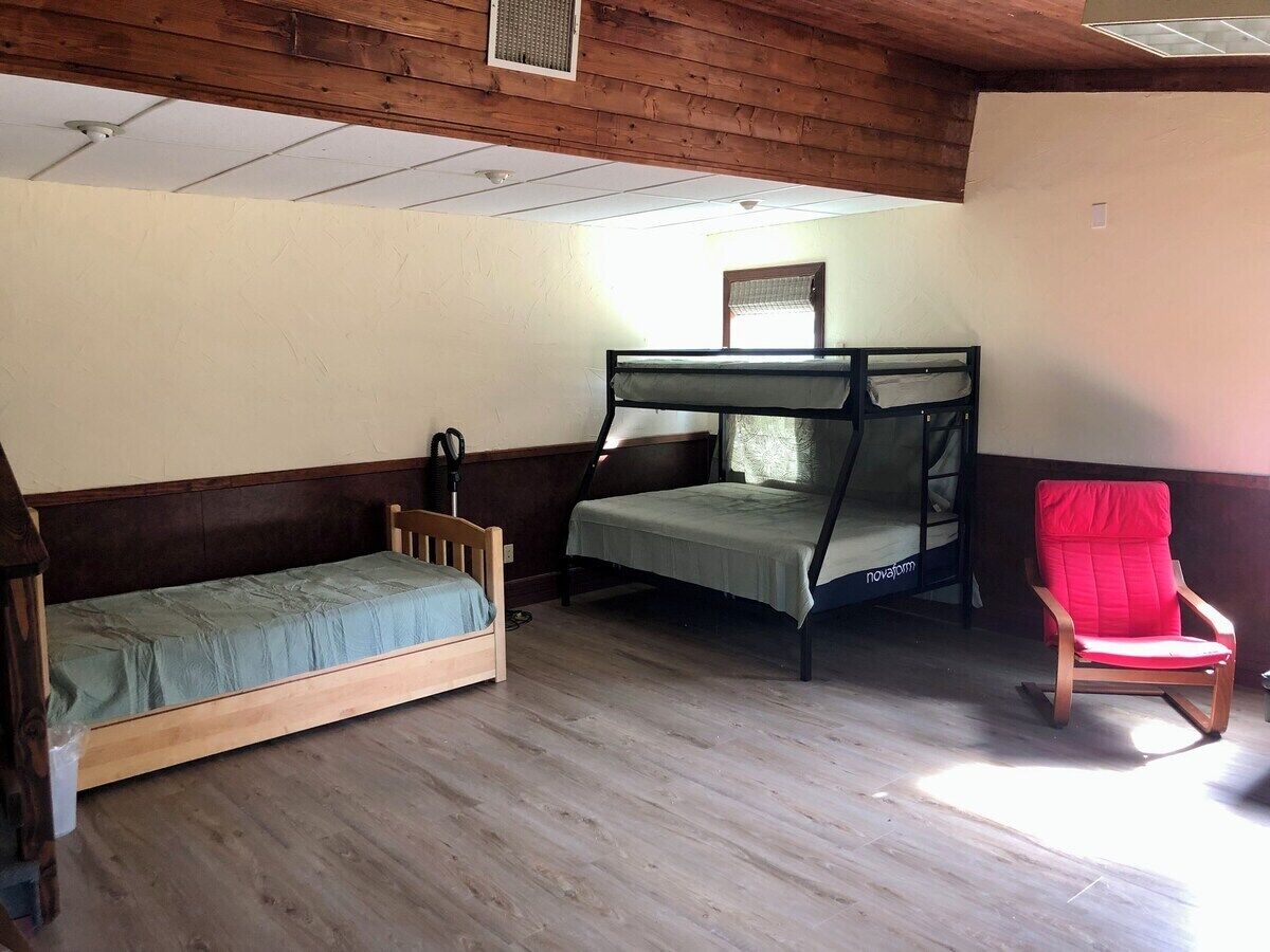A room with a wooden floor, a bunk bed, a single bed, and a red chair.