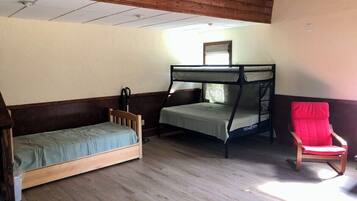 A room with a wooden floor, a bunk bed, a single bed, and a red chair.
