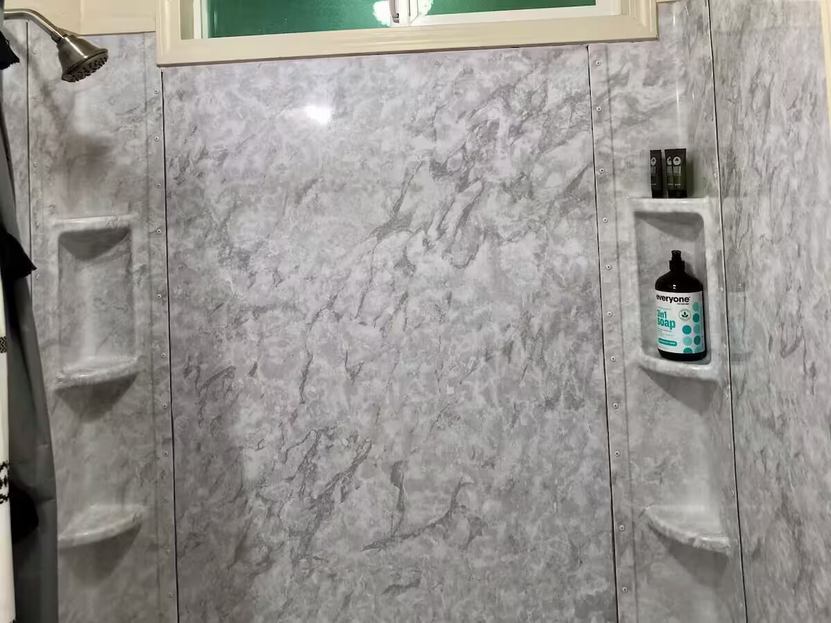 Een badkamer met een douche, een zeepdispenser en een handdoekhouder.