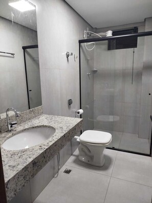 A modern bathroom with a granite countertop sink, a toilet, and a glass-enclosed shower. - Central apartment, 1st floor, with air conditioning, garage, smart TV. (Montes Claros)