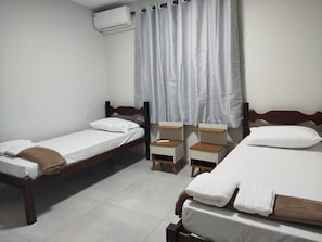 A room with two single beds, a small bedside table with a lamp, and an air conditioning unit on the wall. - Central apartment, 1st floor, with air conditioning, garage, smart TV. (Montes Claros)