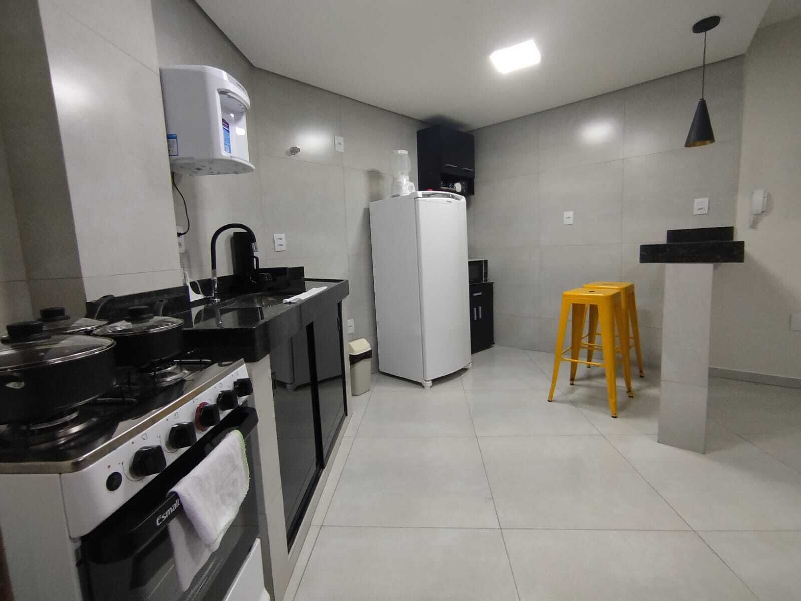 Una cocina compacta con estufa, horno, refrigerador y un taburete pequeño.