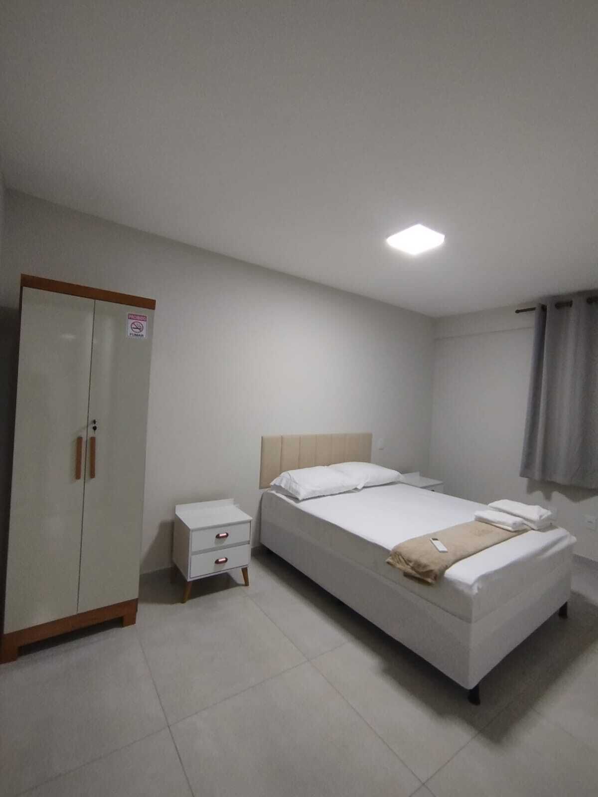 A hotel room with a bed, a wardrobe, a nightstand, and a ceiling light.