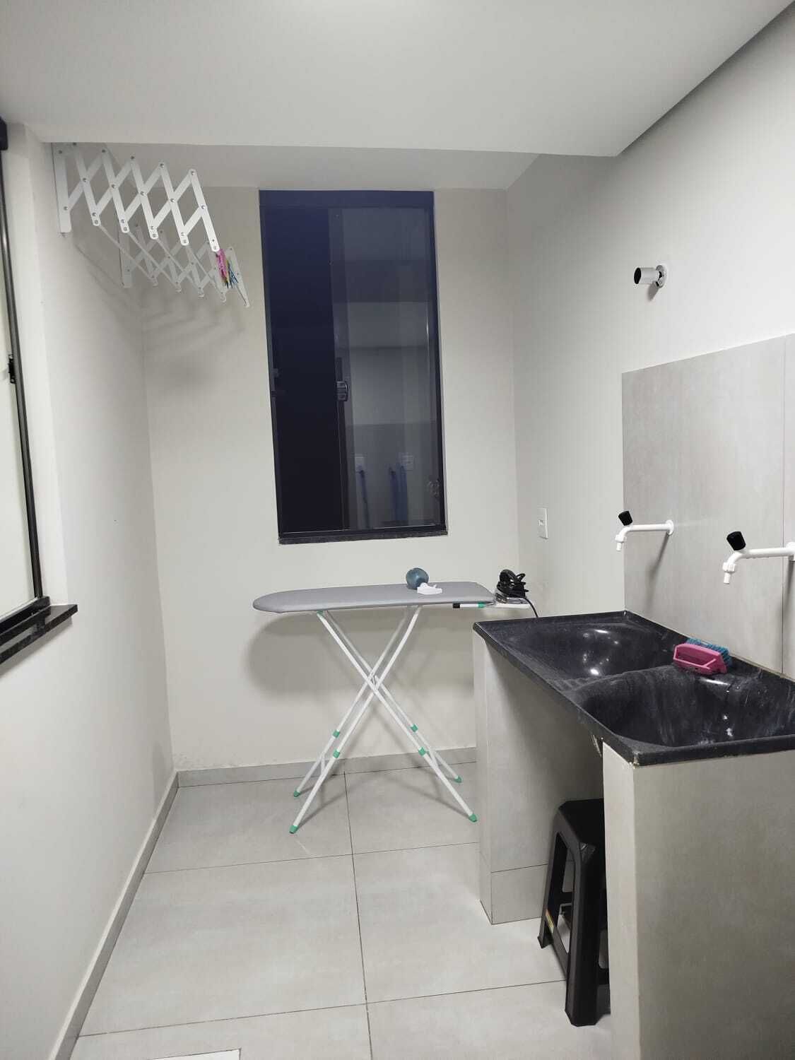 Una cocina compacta con ventana, un tendedero, una tabla de planchar, un lavamanos y un cubo de basura.