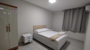 A bedroom with a bed, a nightstand, a wardrobe, and a window with curtains. - Central apartment, 1st floor, with air conditioning, garage, smart TV. (Montes Claros)