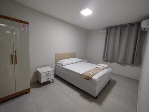 A bedroom with a bed, a nightstand, a wardrobe, and a window with curtains. - Central apartment, 1st floor, with air conditioning, garage, smart TV. (Montes Claros)