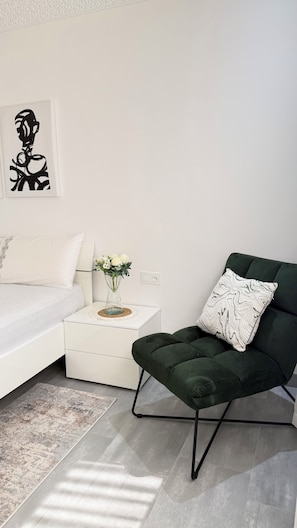 A modern living room with a white sofa, a green armchair, a small white side table with a vase of flowers, and a black abstract painting on the wall. - Elegant Moroccan Apartment | 2 Bedrooms & 2 Bathrooms (Tanger)