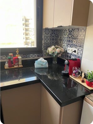 A kitchen with a black countertop, a window, and a patterned backsplash. - Elegant Moroccan Apartment | 2 Bedrooms & 2 Bathrooms (Tanger)