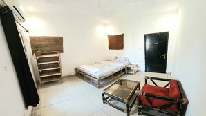 Ett kompakt bostadsutrymme med en säng, ett litet bord, en stol, en hylla med en växt och en dörr.