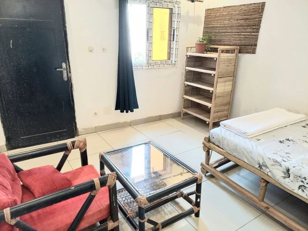 Een kamer met een bed, een tafel, een stoel, een raam met gordijn en een plank met een plant.
