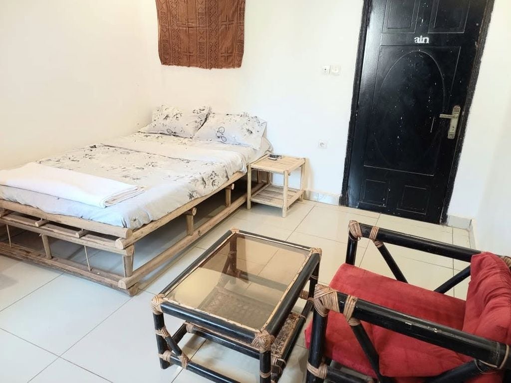 A room with a bed, a small table, a red chair, and a black door.