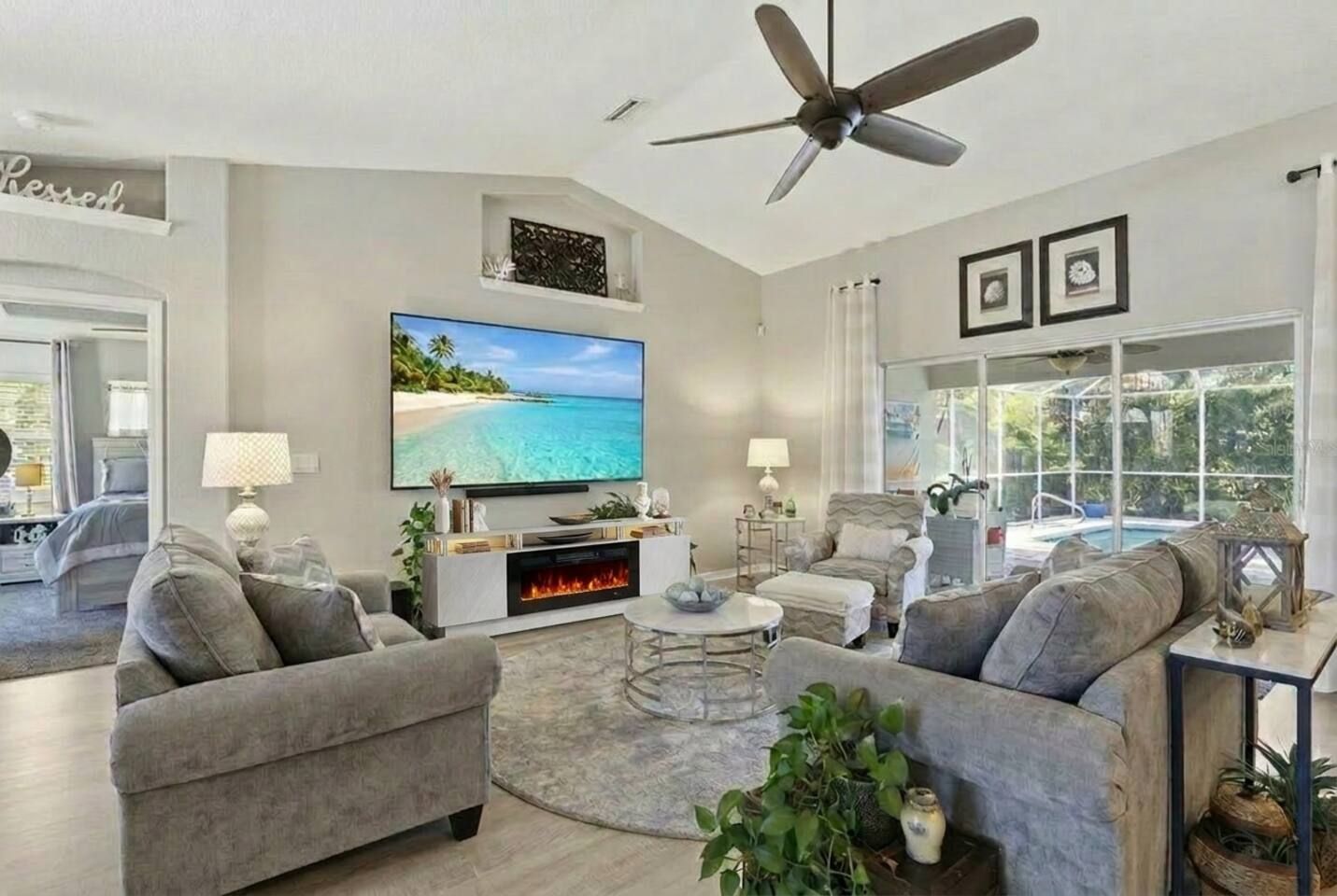 A modern living room with a flat-screen TV, grey sofas, a fireplace, and a ceiling fan.