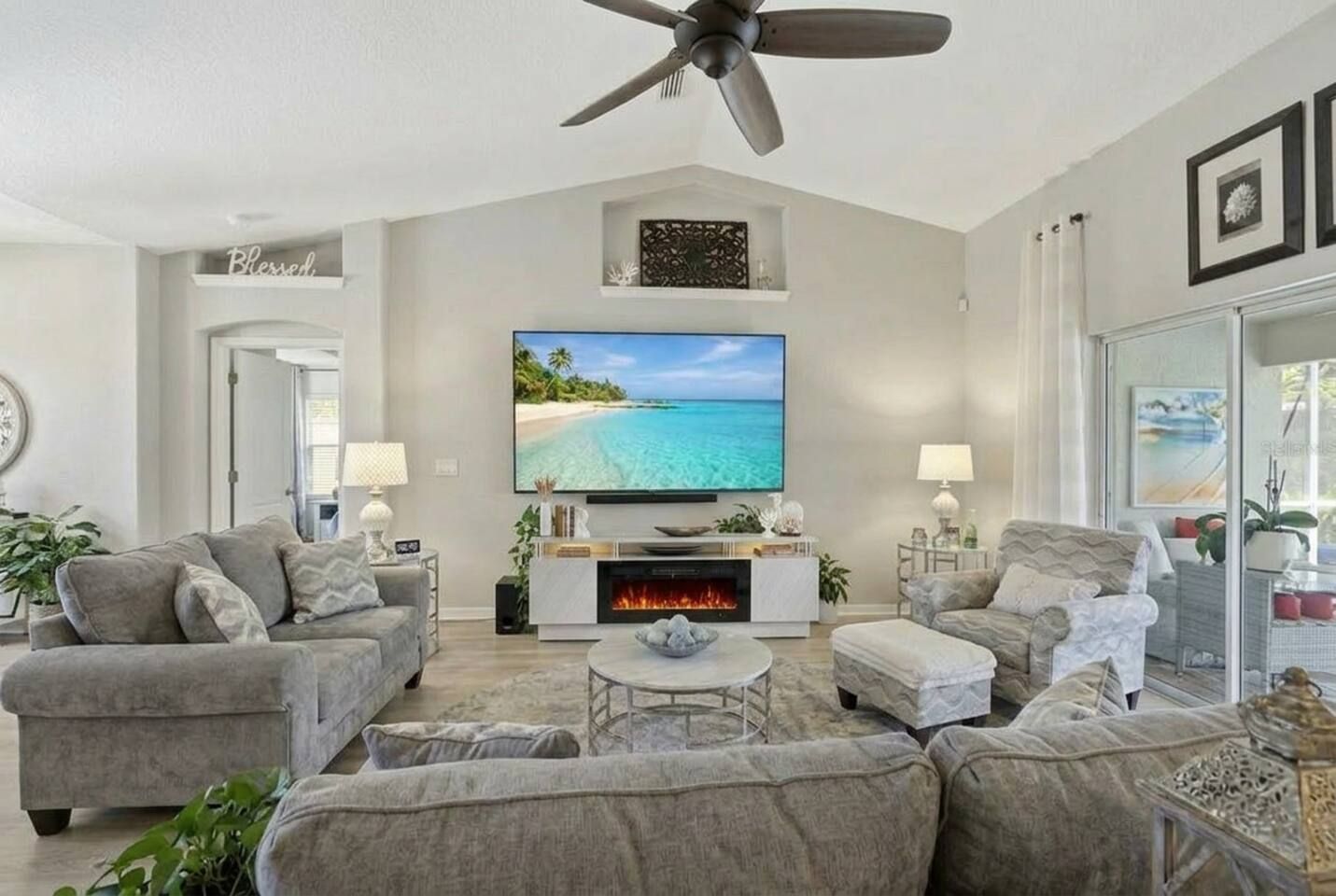 A living room with a fireplace, a ceiling fan, and a large flat-screen TV.
