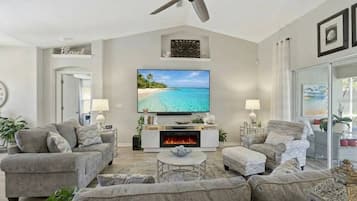A living room with a fireplace, a ceiling fan, and a large flat-screen TV.