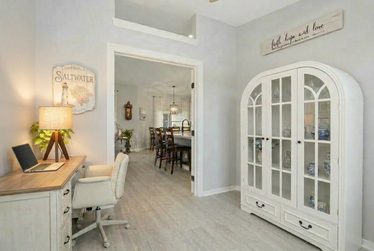 Una habitación con escritorio, silla, lámpara y aparador con puertas de cristal.