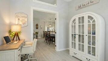 Una habitación con escritorio, silla, lámpara y aparador con puertas de cristal.