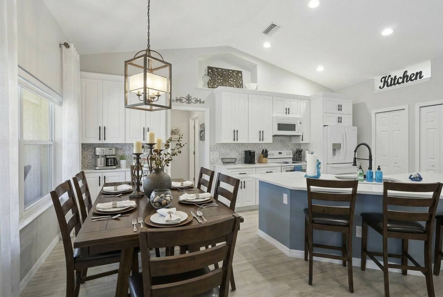 A modern kitchen with white cabinetry, a central island, and a dining area with wooden chairs.
