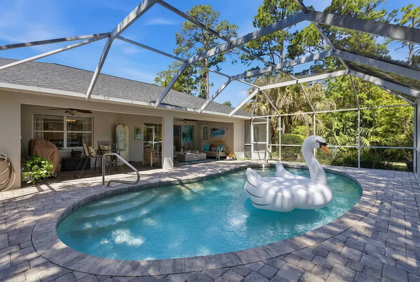 A swimming pool with a swan float, a covered patio area, and a view of trees.