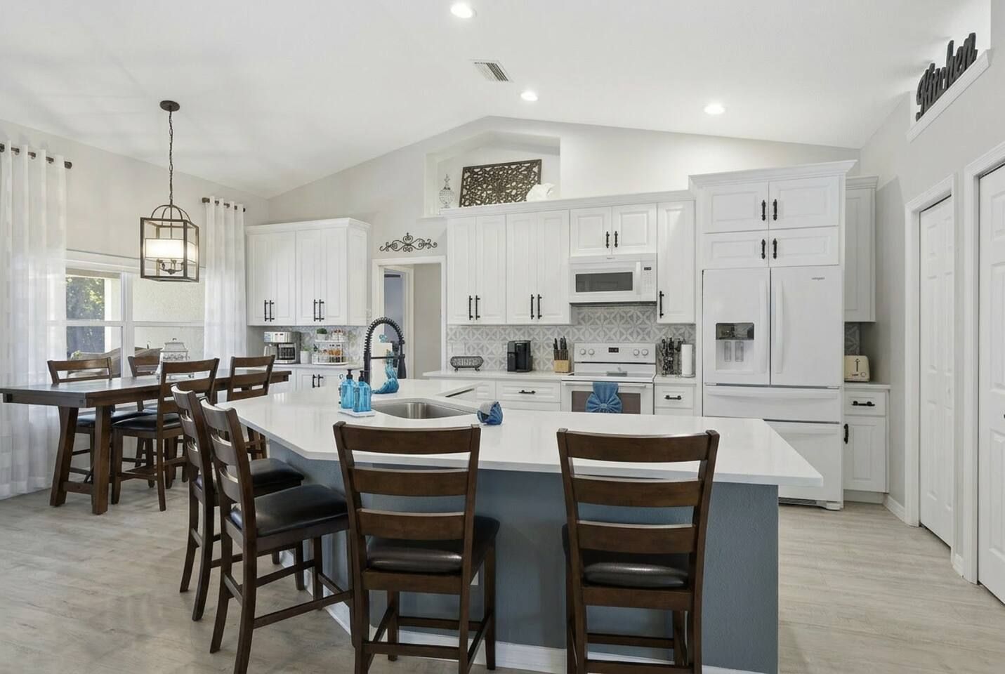 Una cocina moderna con armarios blancos, una isla central y un comedor con sillas de madera.