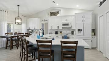 Una cocina moderna con armarios blancos, una isla central y un comedor con sillas de madera.