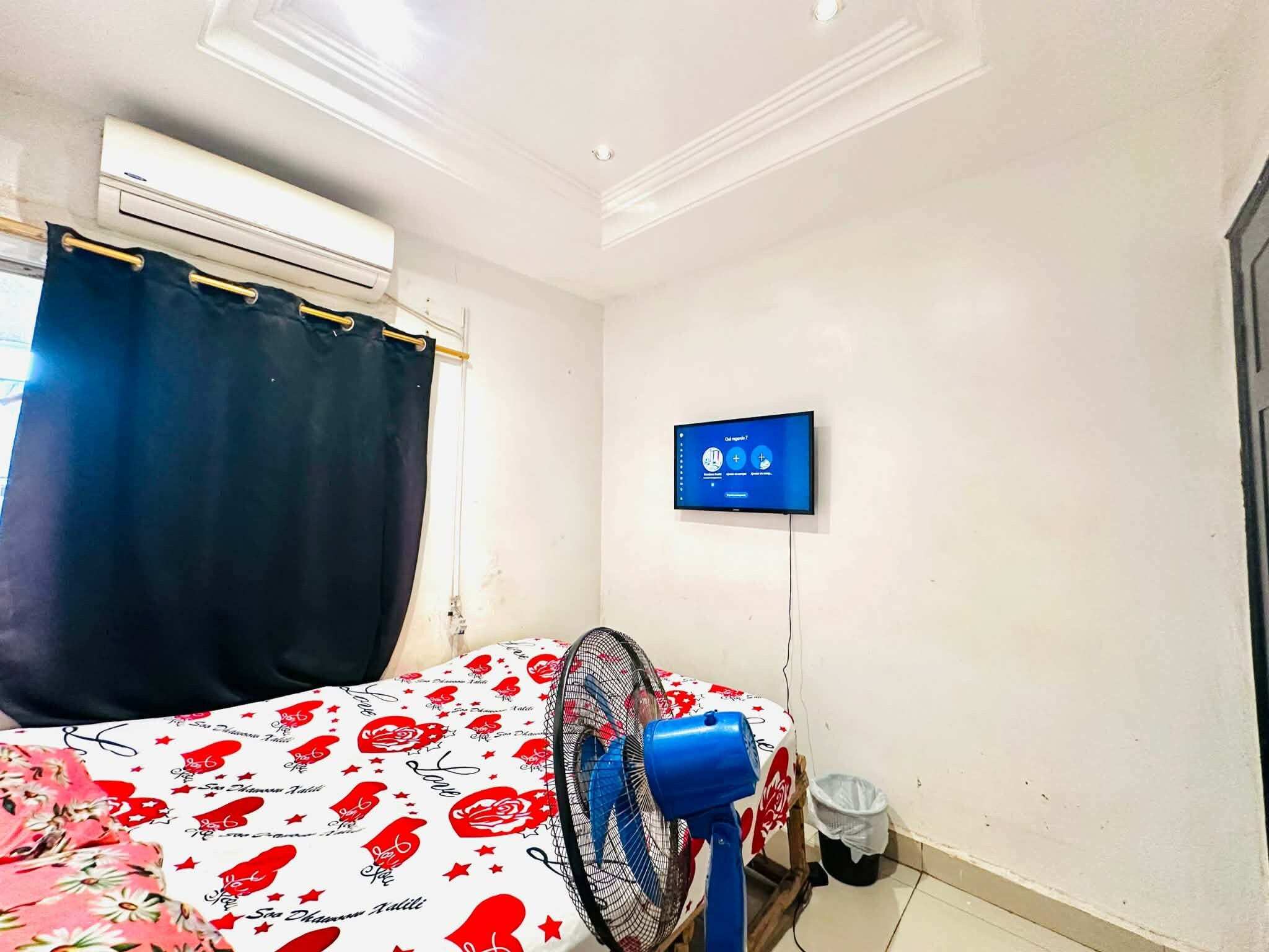 Una habitación con una cama, un televisor de pared, un ventilador de techo y un equipo de aire acondicionado.