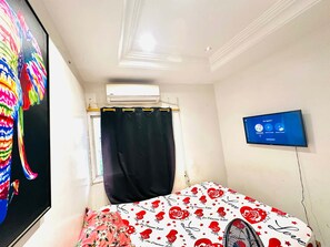 A bedroom with a bed, a TV, an air conditioning unit, and a window with a curtain. - Room-beautiful Room With Private Toilet (Bamako)