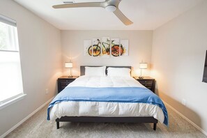 Quarto com cama, duas mesas de cabeceira, ventilador de teto e uma obra de arte na parede.