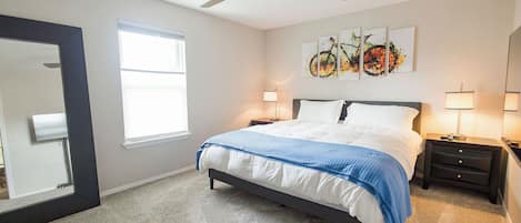 Un dormitorio con una cama, dos mesitas de noche, un ventilador de techo, un ventanal y obras de arte en la pared.