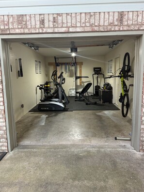 A home gym with exercise equipment, a bicycle, and a door leading to another room. - Ride-Out-the-Door to Slaughter Pen- Hot Tub, Sauna & Gym 10 min to OZ Bike Park (Bentonville)