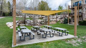 Zona de picnic al aire libre con varias mesas y una vela de sombra amarilla.