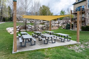 Zona de picnic al aire libre con varias mesas y una vela de sombra amarilla.