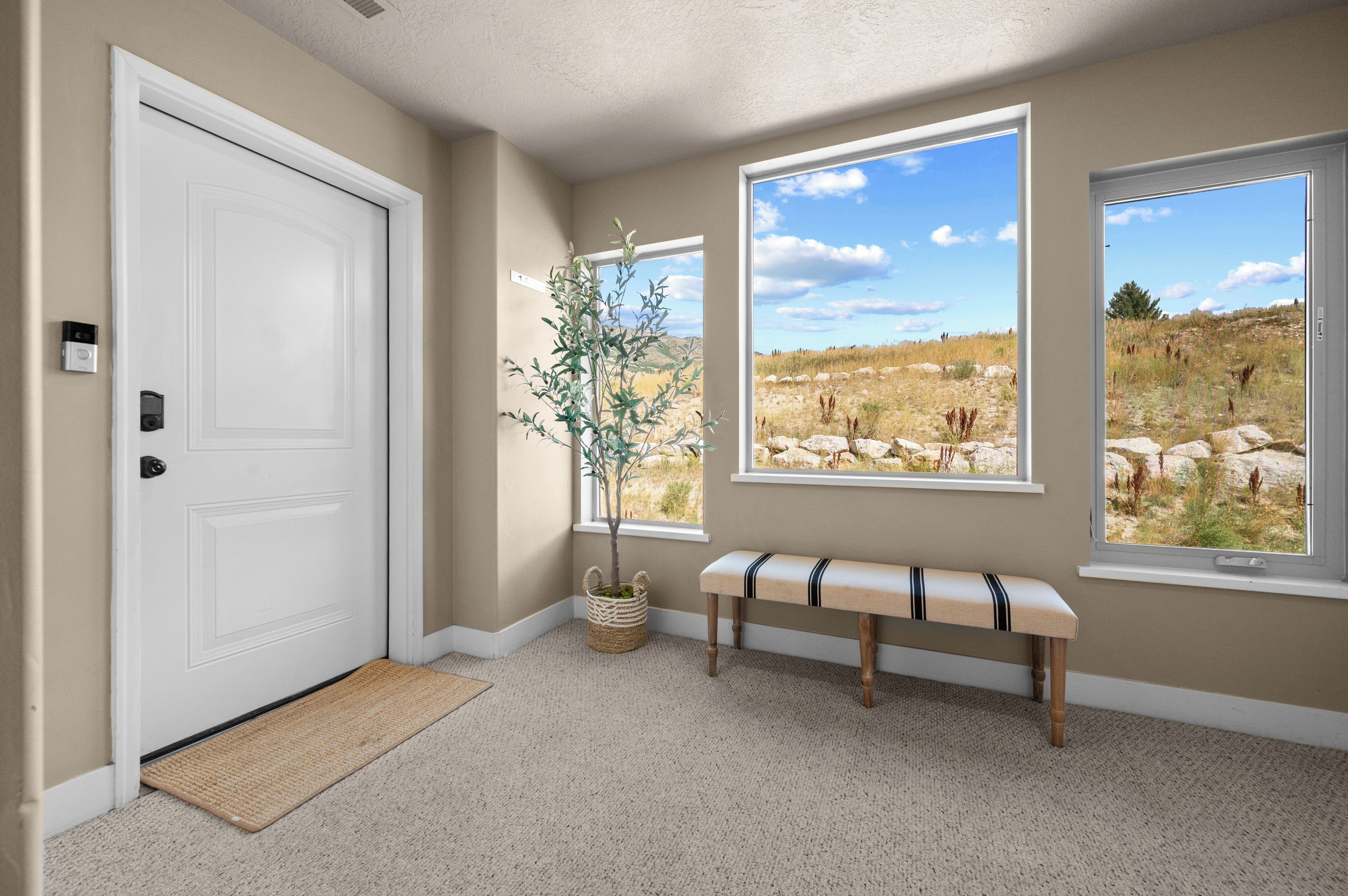 Un pasillo con una puerta blanca, un banco y dos ventanas que dan a un paisaje cubierto de césped.