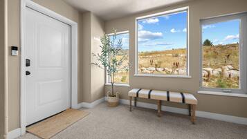 Un pasillo con una puerta blanca, un banco y dos ventanas que dan a un paisaje cubierto de césped.