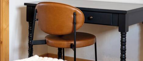 Una silla con asiento y respaldo de cuero, ubicada frente a un escritorio con cajón.